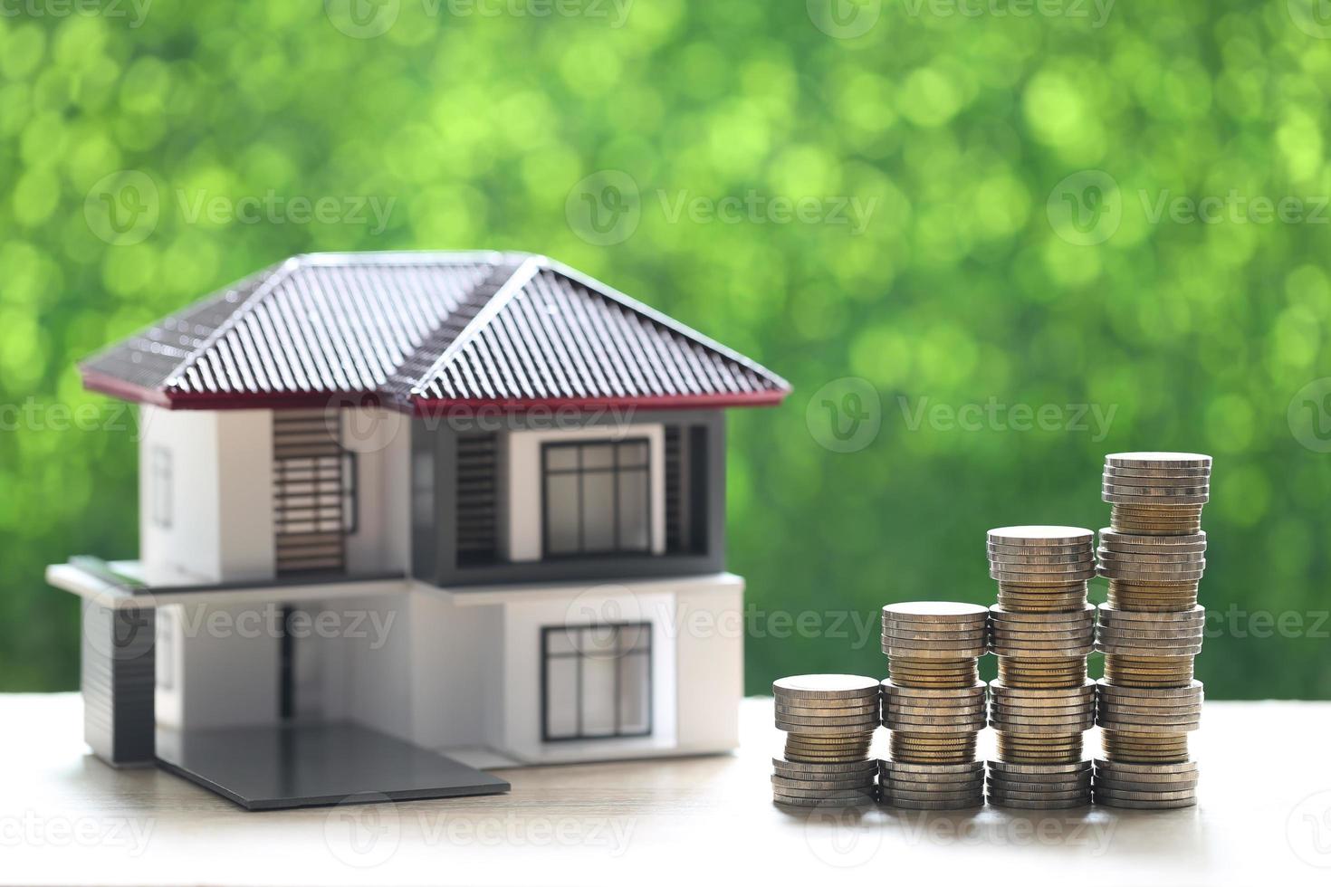 Modellhaus und Stapel von Geldmünzen auf natürlichem grünem Hintergrund foto