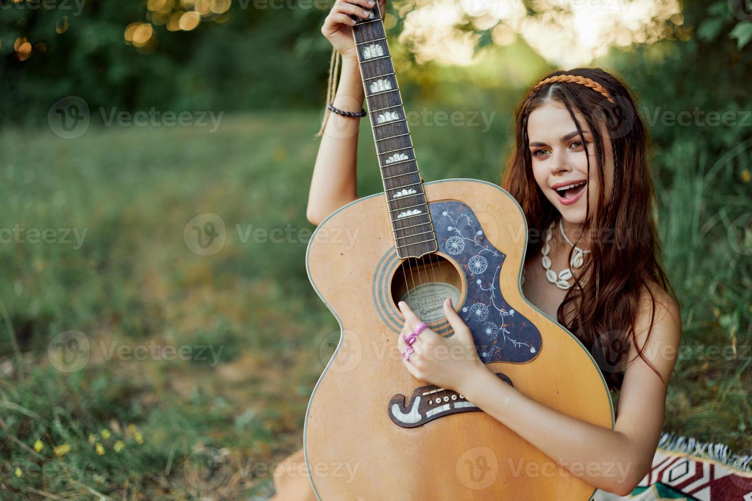 schön Frau spielen Gitarre im Natur im ein Hippie Sommer- sehen, Singen Lieder Stil von Leben ohne Sorgen foto