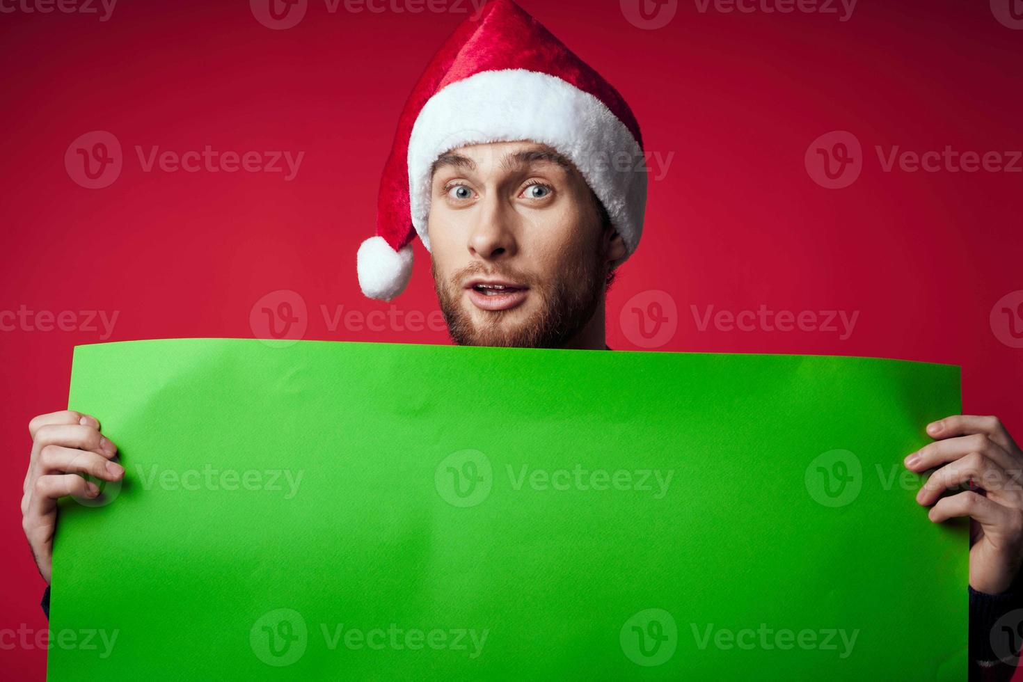 gut aussehend Mann im ein Santa Hut halten ein Banner Urlaub rot Hintergrund foto