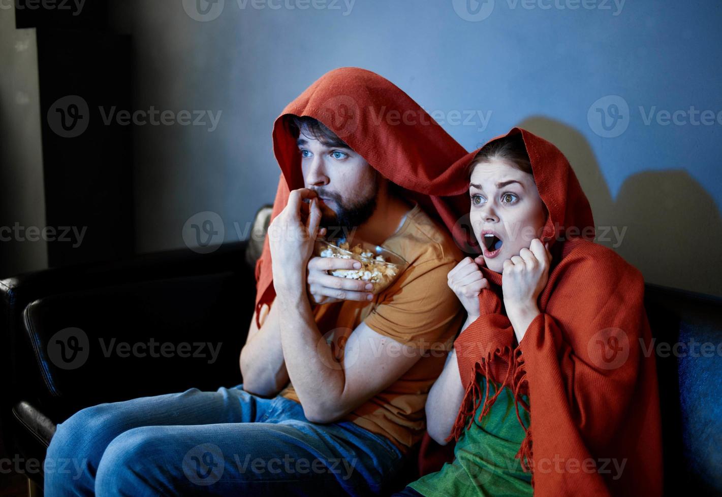 ein Mann und ein Frau mit ein rot Plaid auf ihr Köpfe sind Sitzung auf das Sofa im Vorderseite von das Fernseher drinnen foto