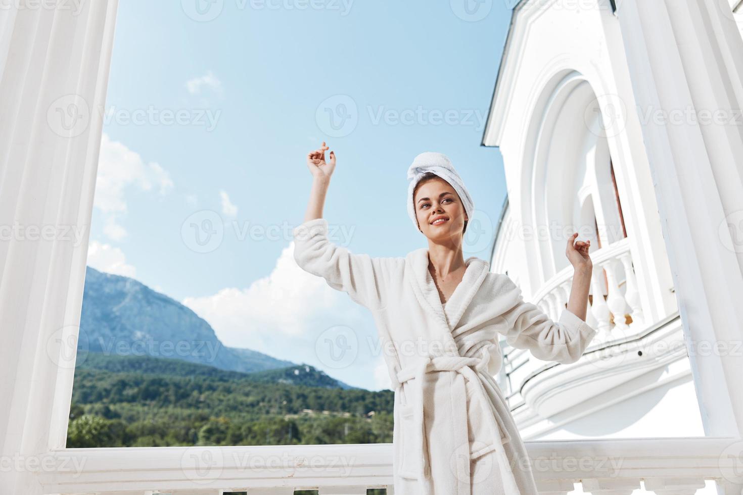 Frau mit Hände angehoben oben und im ein Weiß Kleid auf das Balkon gegen das Hintergrund von Berge foto