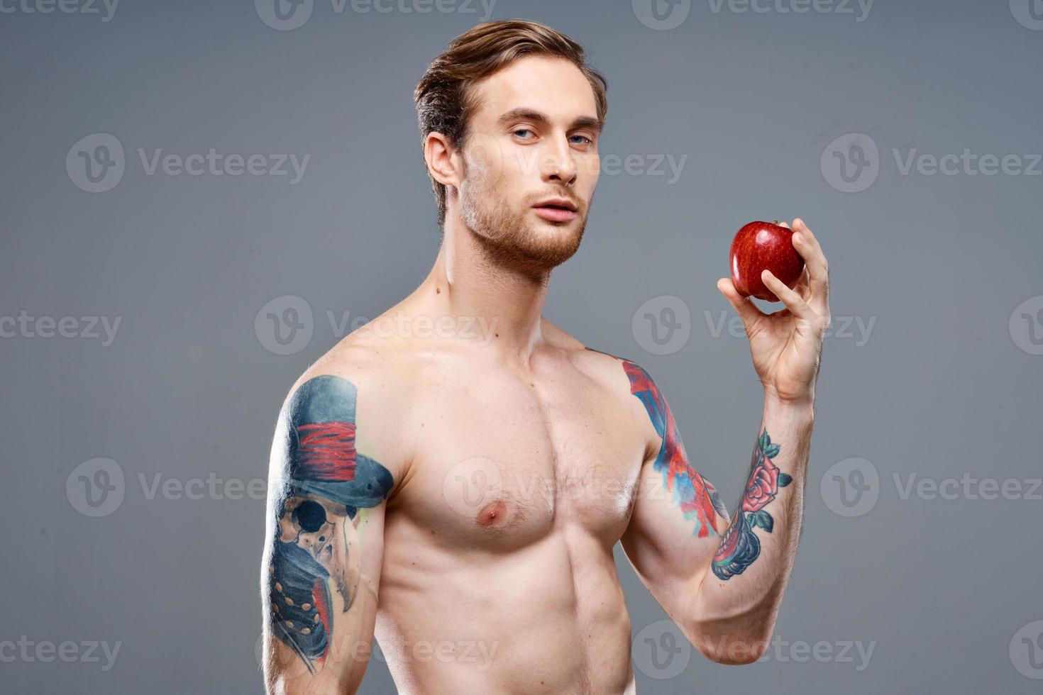 sportlich Mann mit ein aufgepumpt Torso und ein tätowieren auf seine Arm rot Apfel Gesundheit foto