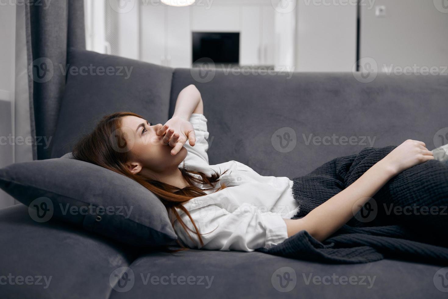 Frau halten ihr Hand auf ihr Gesicht Lügen auf das Couch versteckt hinter ein Decke Gefühl nicht wohl foto