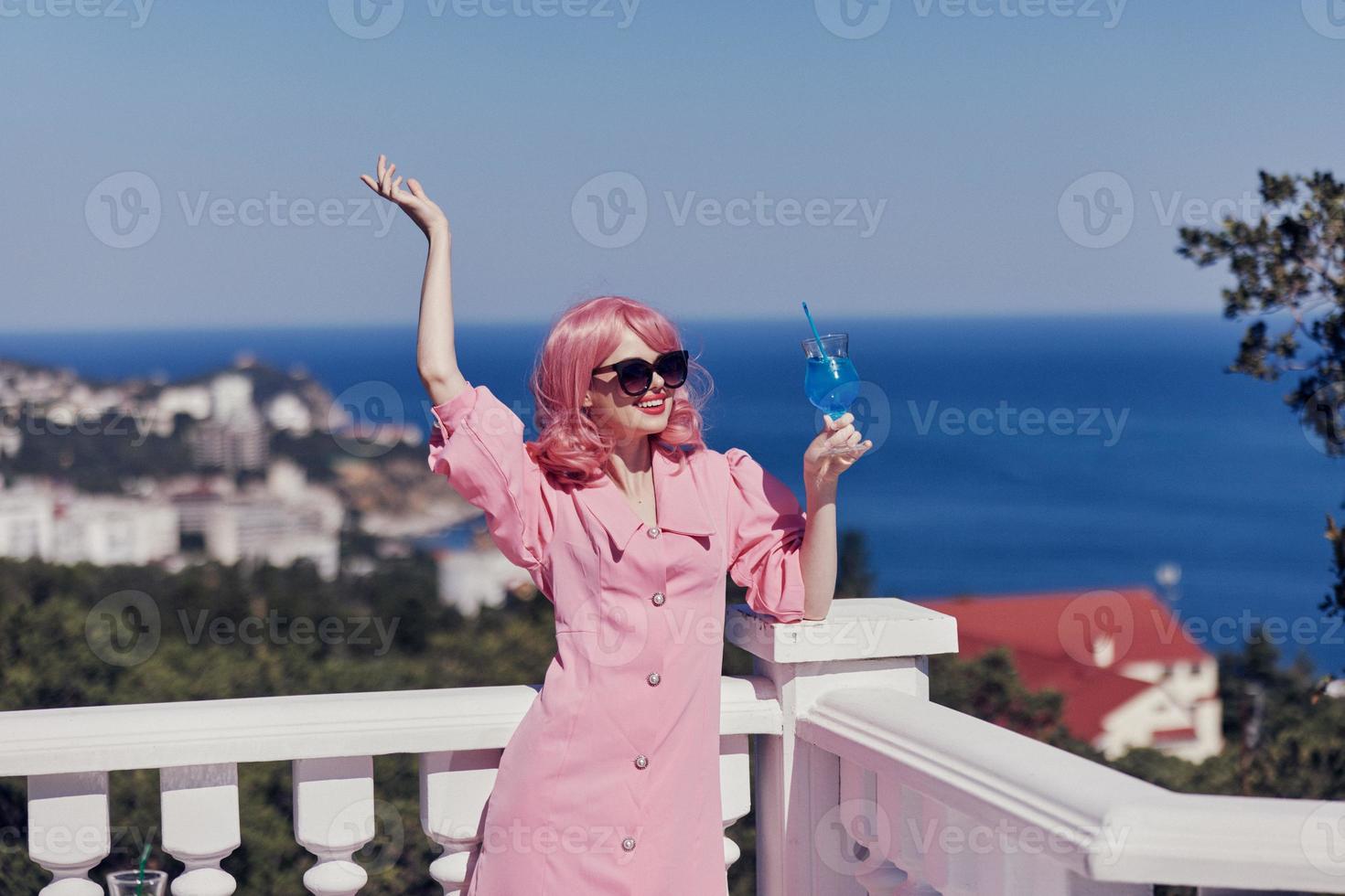 Erfreut jung Mädchen im ein Rosa Kleid im Sonnenbrille mit ein Cocktail unverändert foto