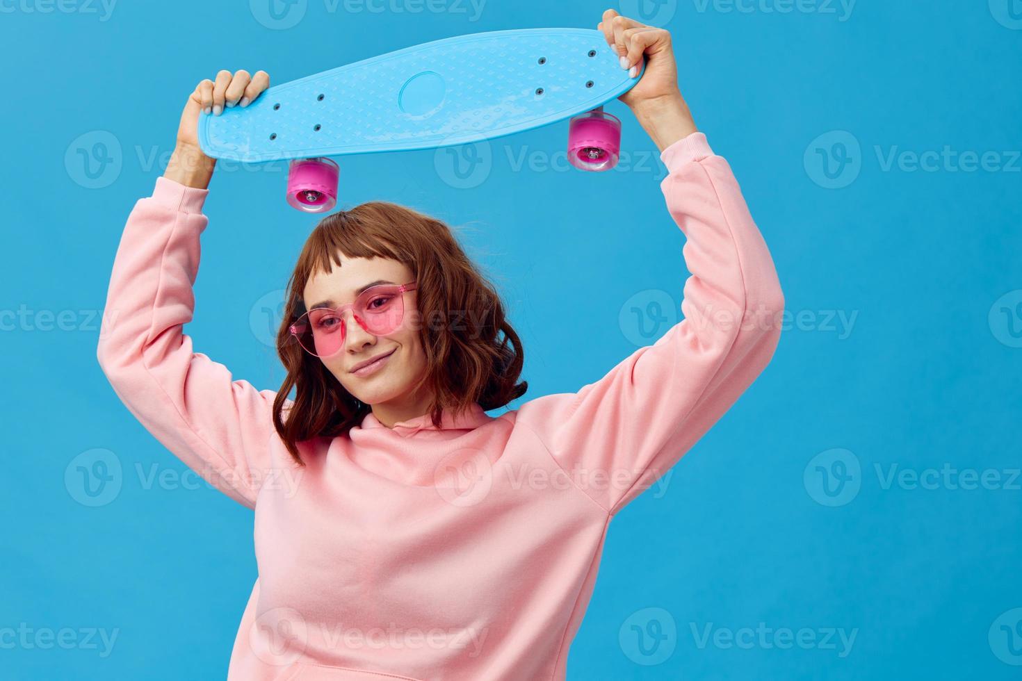 glücklich heiter ziemlich Rothaarige Dame im Rosa Kapuzenpullover Sonnenbrille mit Penny Tafel posieren isoliert auf Blau Studio Hintergrund. Kopieren Raum Banner Angebot. Mode Kino. Urlaub Aktivität Konzept foto