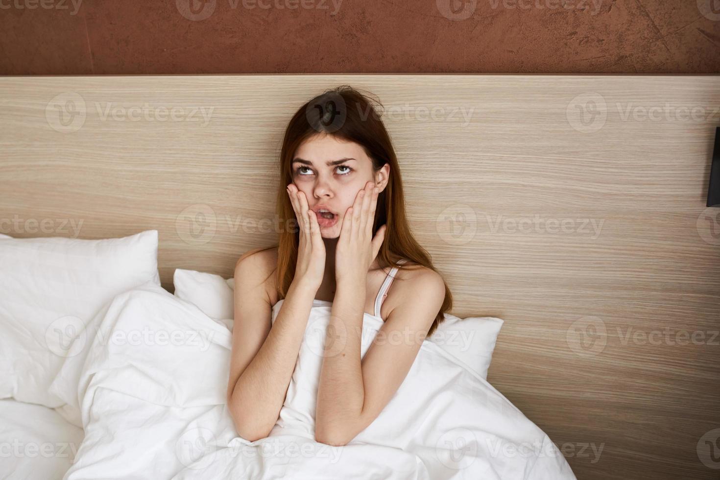 Frau wachte auf oben früh im das Morgen und berühren ihr Gesicht mit ihr Hände unter das Abdeckungen im Bett foto