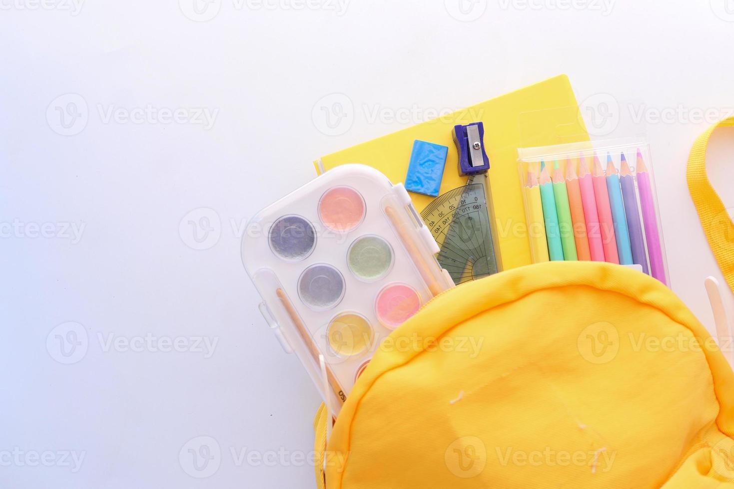 gelber Rucksack und Schulmaterial auf weißem Hintergrund foto