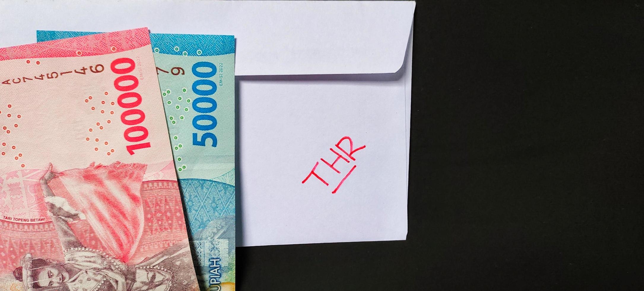 ein Weiß Briefumschlag geschrieben von thr und Neu indonesisch Banknoten, in der Regel Tunjangan Hari raya oder namens thr sind gegeben zu Angestellte voraus von eid. isoliert auf ein schwarz Hintergrund foto
