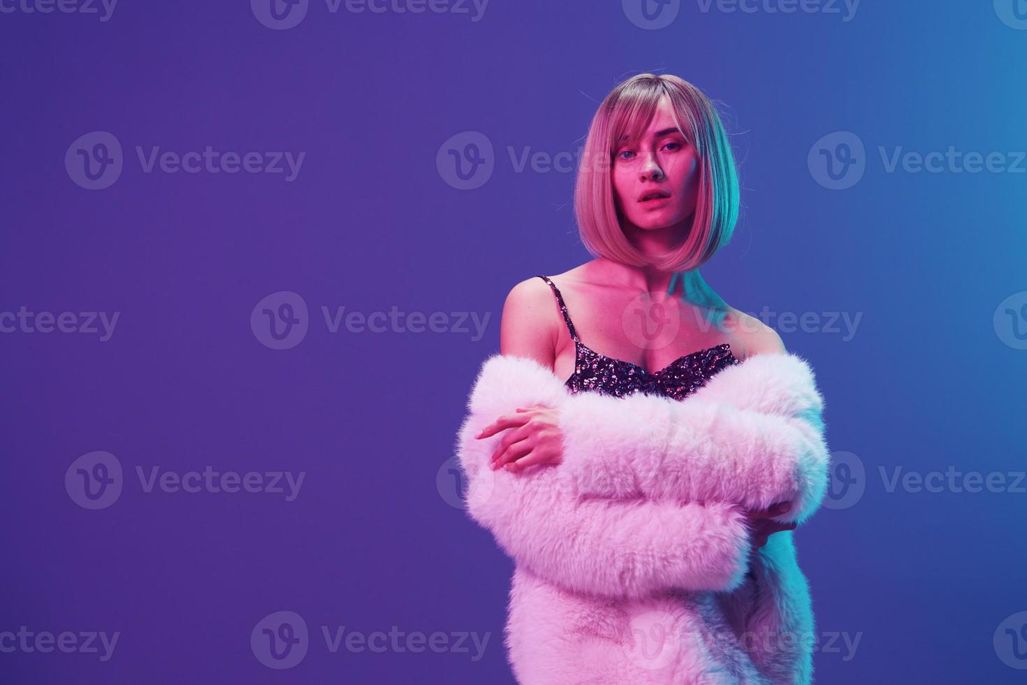 sexy blond Frau im flauschige Pelz Mantel prickelnd Kleid mit öffnen Schultern Kreuz Hände posieren isoliert im Blau violett Rosa Farbe Licht Studio Hintergrund. Neon- Party Mode Konzept. Kopieren Raum Banner foto