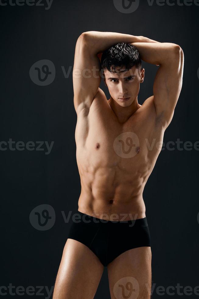 sportlich Mann mit ein aufgepumpt muskulös Körper hält seine Hände über seine Kopf posieren Macho dunkel Hintergrund foto