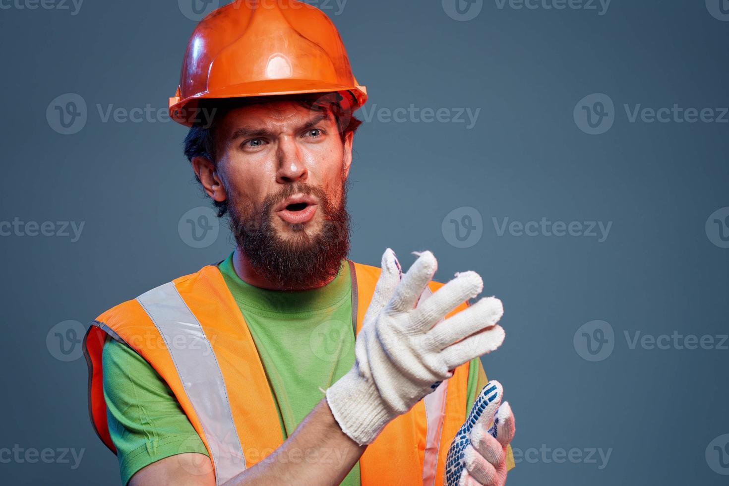 bärtig Mann im Orange schwer Hut Handschuhe Fachmann abgeschnitten Aussicht Blau Hintergrund foto