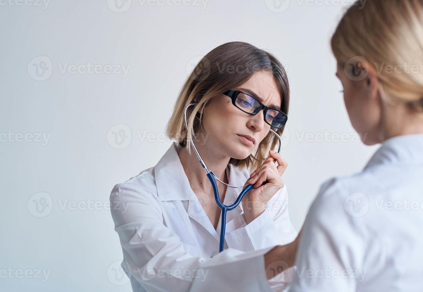 Frau Reinigung Dame im ein medizinisch Kleid hört zu zu das Patienten Herzschlag auf ein Licht Hintergrund foto