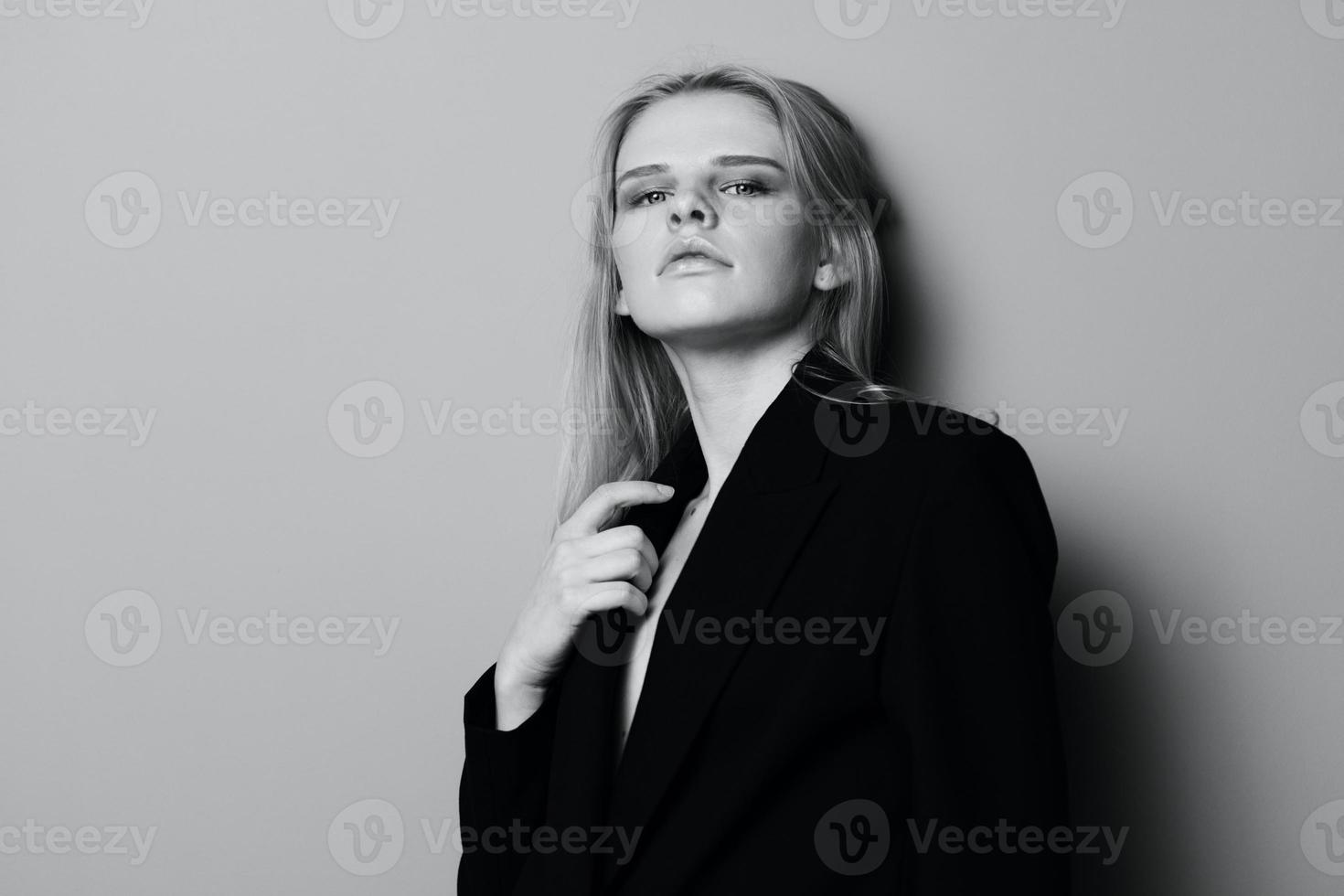 Herrlich jung stilvoll Dame im Jacke posieren gelehnt auf das Mauer beim Studio. ziemlich weiblich blond Modell- sexy suchen beim Kamera foto