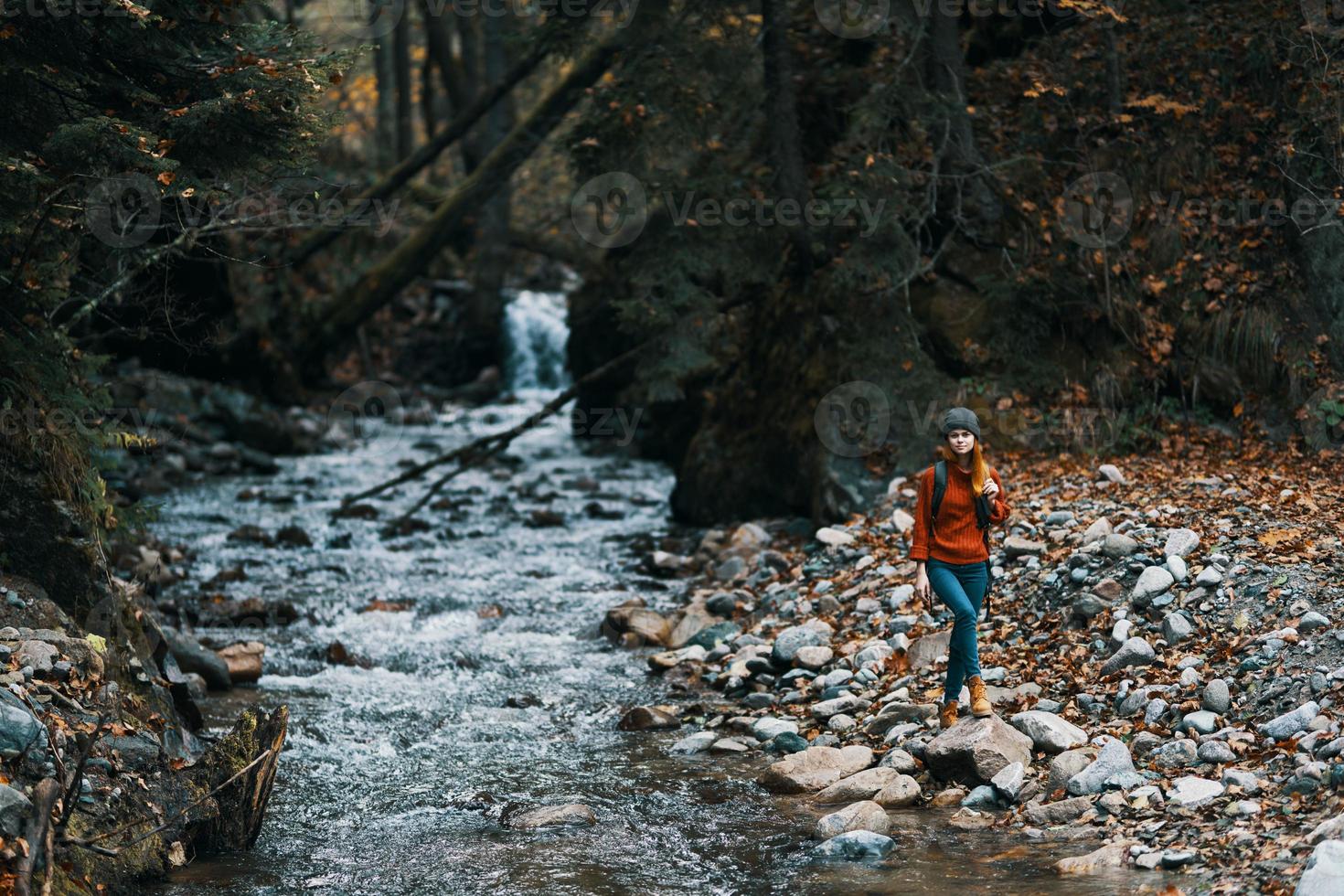 Frau Reisen durch das Fluss im das Berge und ein Rucksack auf ihr zurück transparent Wasser Wald foto