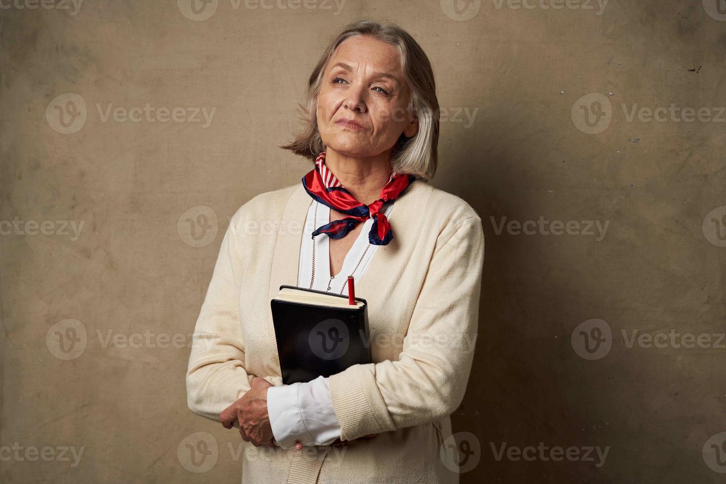 Alten Frau im ein Dressing Kleid mit ein Notizbuch im ihr Hände Studio Arbeit foto