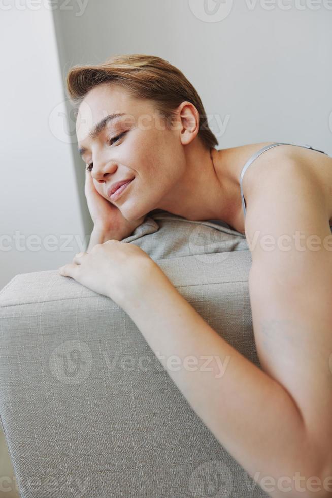 glücklich Frau Lächeln Lügen beim Zuhause auf das Couch entspannend auf ein Wochenende beim Zuhause mit ein kurz Haarschnitt Haar ohne Filter auf ein Weiß Hintergrund, kostenlos Kopieren Raum foto