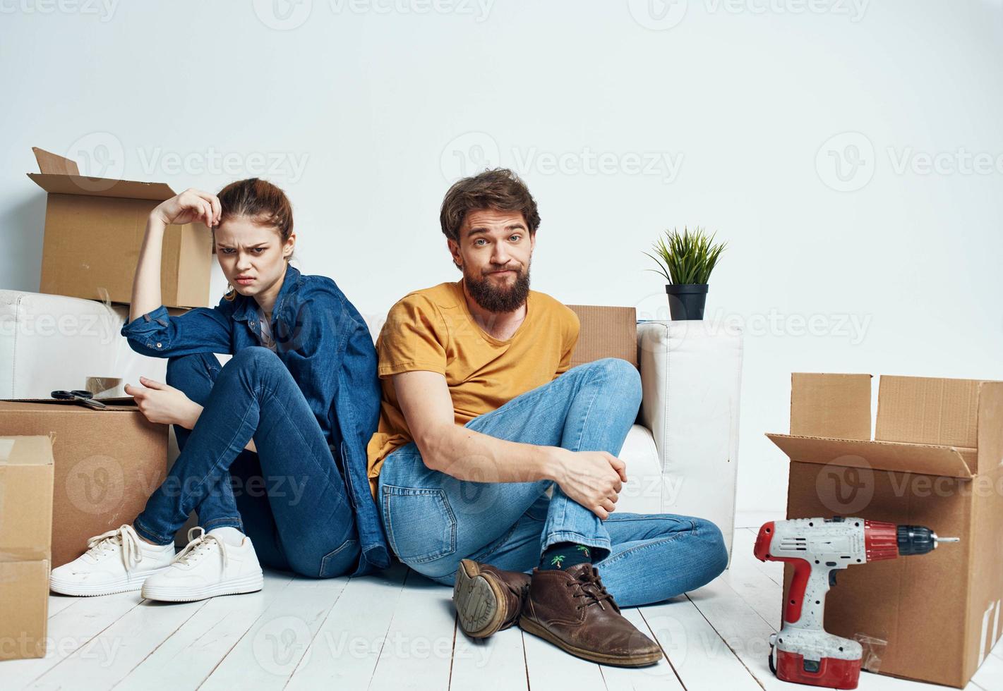 ein Mann und ein Frau sind Sitzung auf das Fußboden mit öffnen Kisten und Werkzeuge zum Reparatur foto