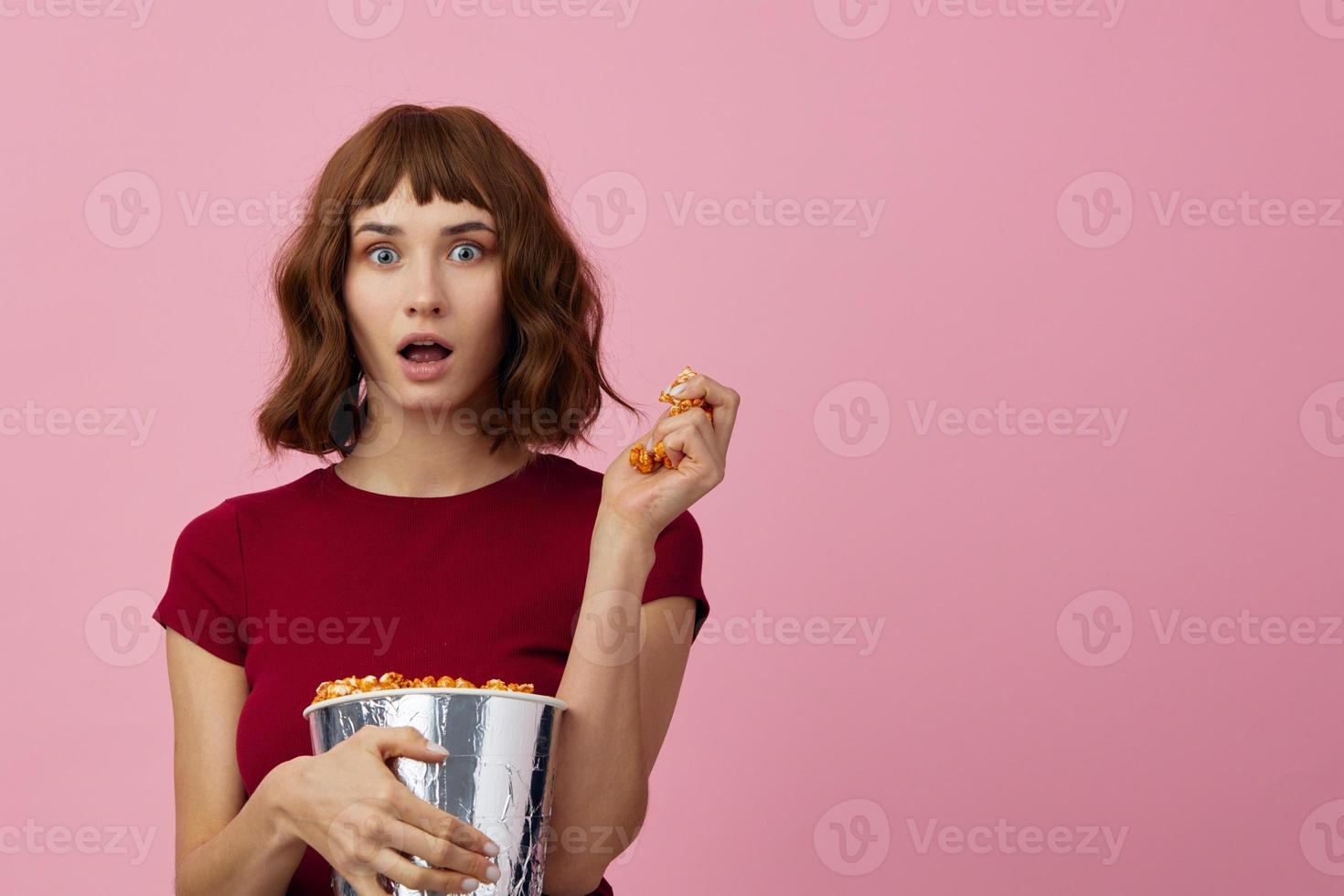 aufgeregt schockiert süß Rothaarige Dame im rot T-Shirt mit Popcorn bereit zum Film Abend posieren isoliert auf Über Rosa Studio Hintergrund. Kopieren Raum Banner. Mode Kino Konzept. Unterhaltung Angebot foto