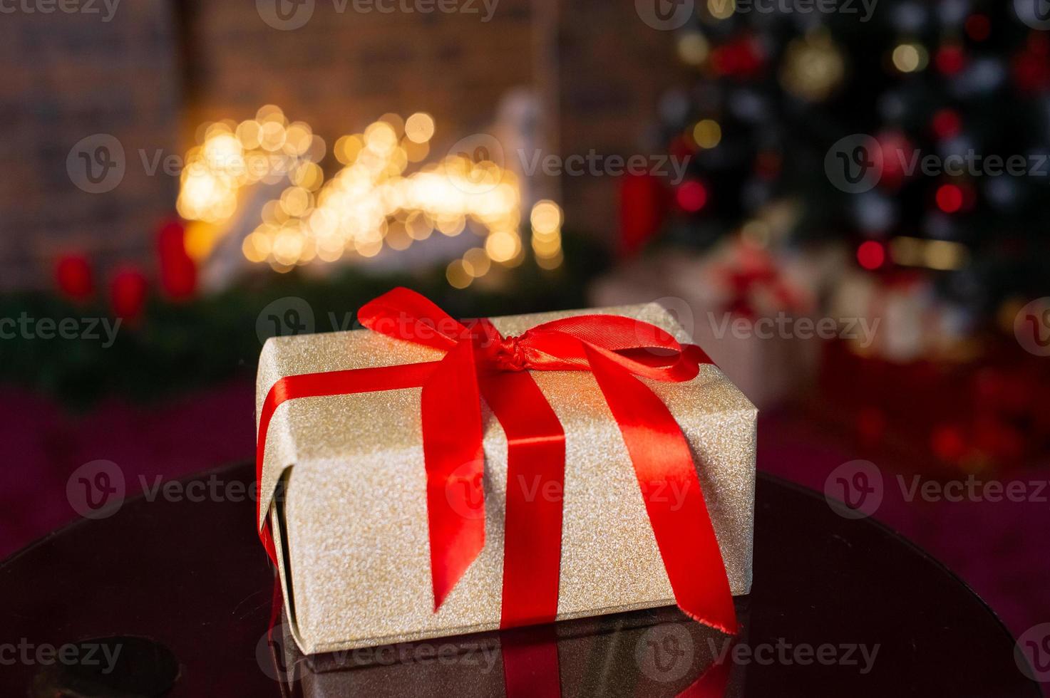 golden Geschenk Box gebunden mit ein rot Band mit ein Bogen auf das Hintergrund von ein Weihnachten Baum foto