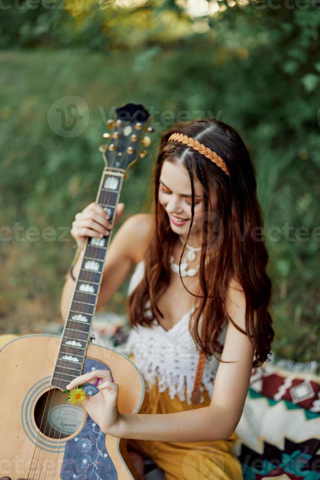 glücklich Hippie Frau mit ein Gitarre entspannend im Natur Sitzung auf ein Plaid lächelnd und genießen das Sicht. Lebensstil im Harmonie mit Natur und selbst foto