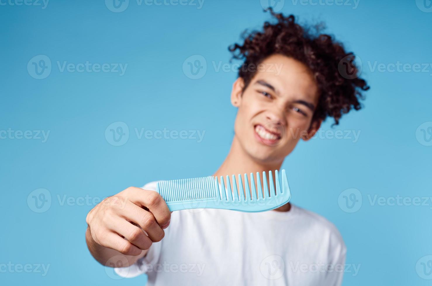 glücklich Kerl mit ein Kamm im seine Hand auf ein Blau Hintergrund und lockig Haar Brünette Modell- foto