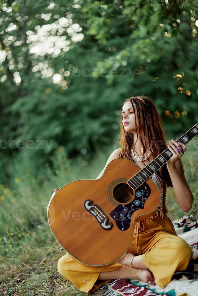 ein Mädchen im Öko-Kleidung Hippie Sitzung mit ein Gitarre und suchen beim ein Sonnenuntergang im das Sommer- foto