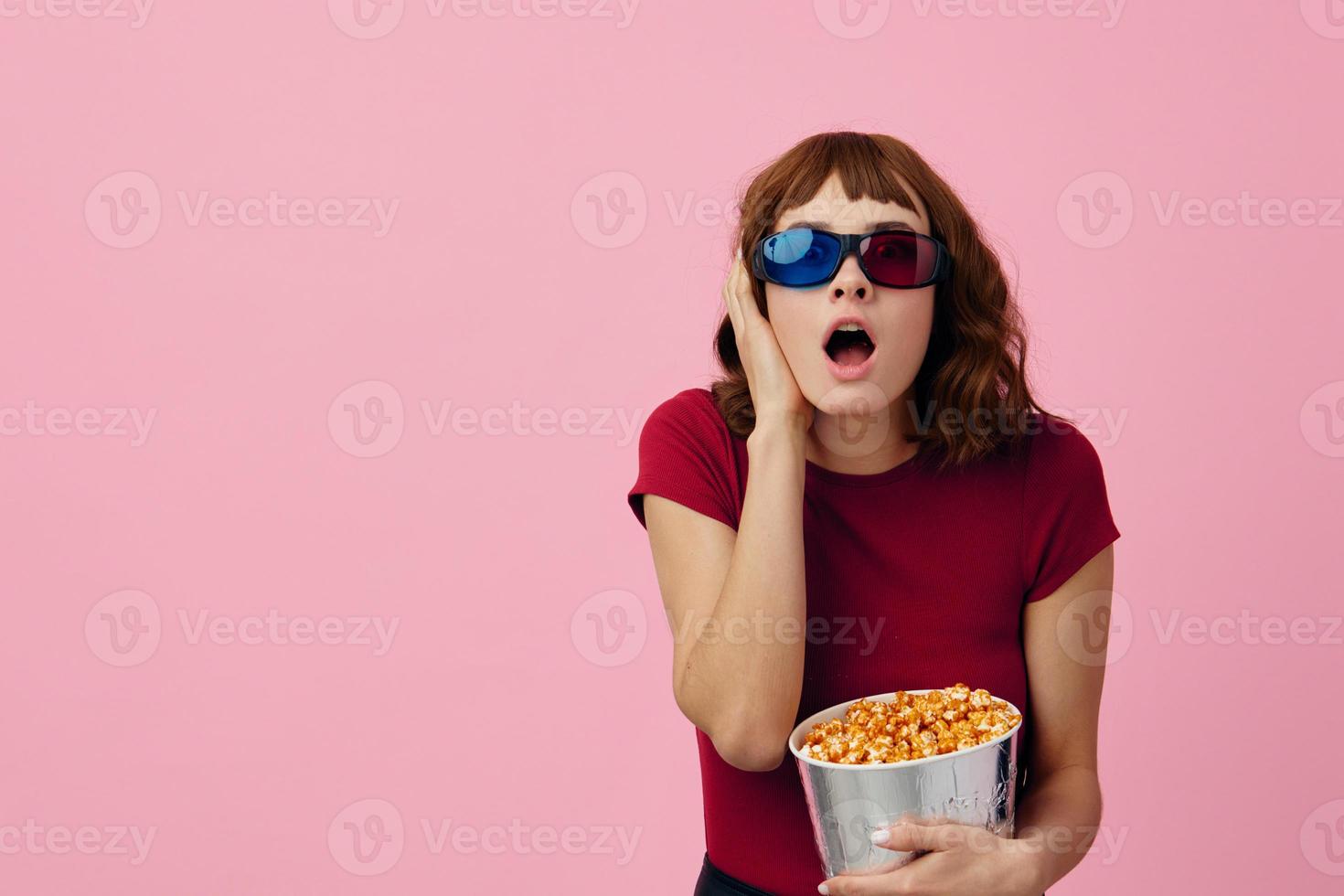 verwirrt konzentriert süß Rothaarige Dame im rot T-Shirt 3d Brille Essen Popcorn Uhr Film posieren isoliert auf Über Rosa Studio Hintergrund. Kopieren Raum Banner. Mode Kino Konzept. Unterhaltung Angebot foto