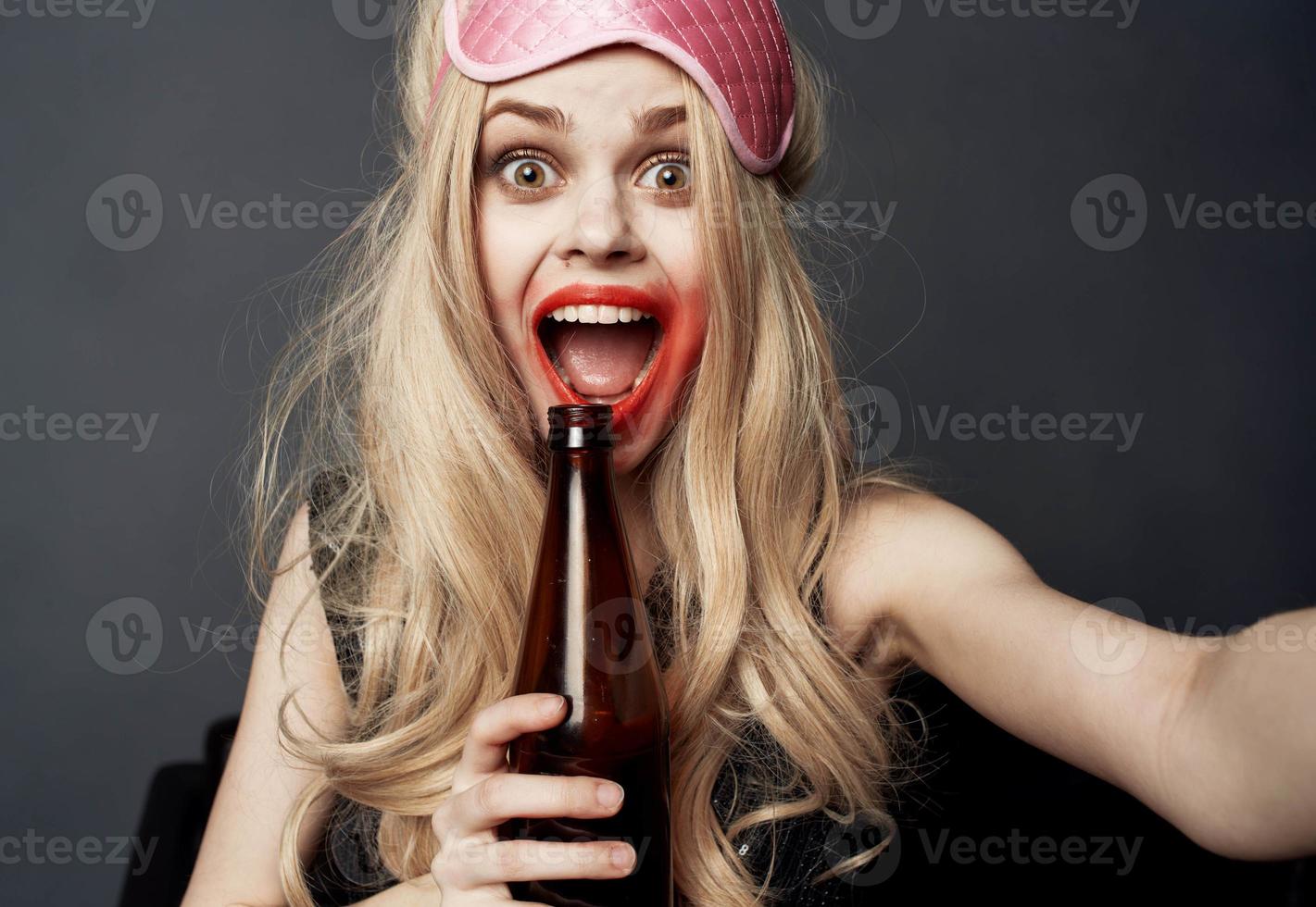 betrunken Frau mit ein Flasche von Bier auf ein grau Hintergrund Gesten mit ihr Hände und hell bilden foto