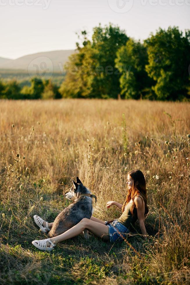 Frau Sitzung im ein Feld mit ein Dackel Hund lächelnd während Ausgaben Zeit im Natur mit ein Freund Hund im Herbst beim Sonnenuntergang foto