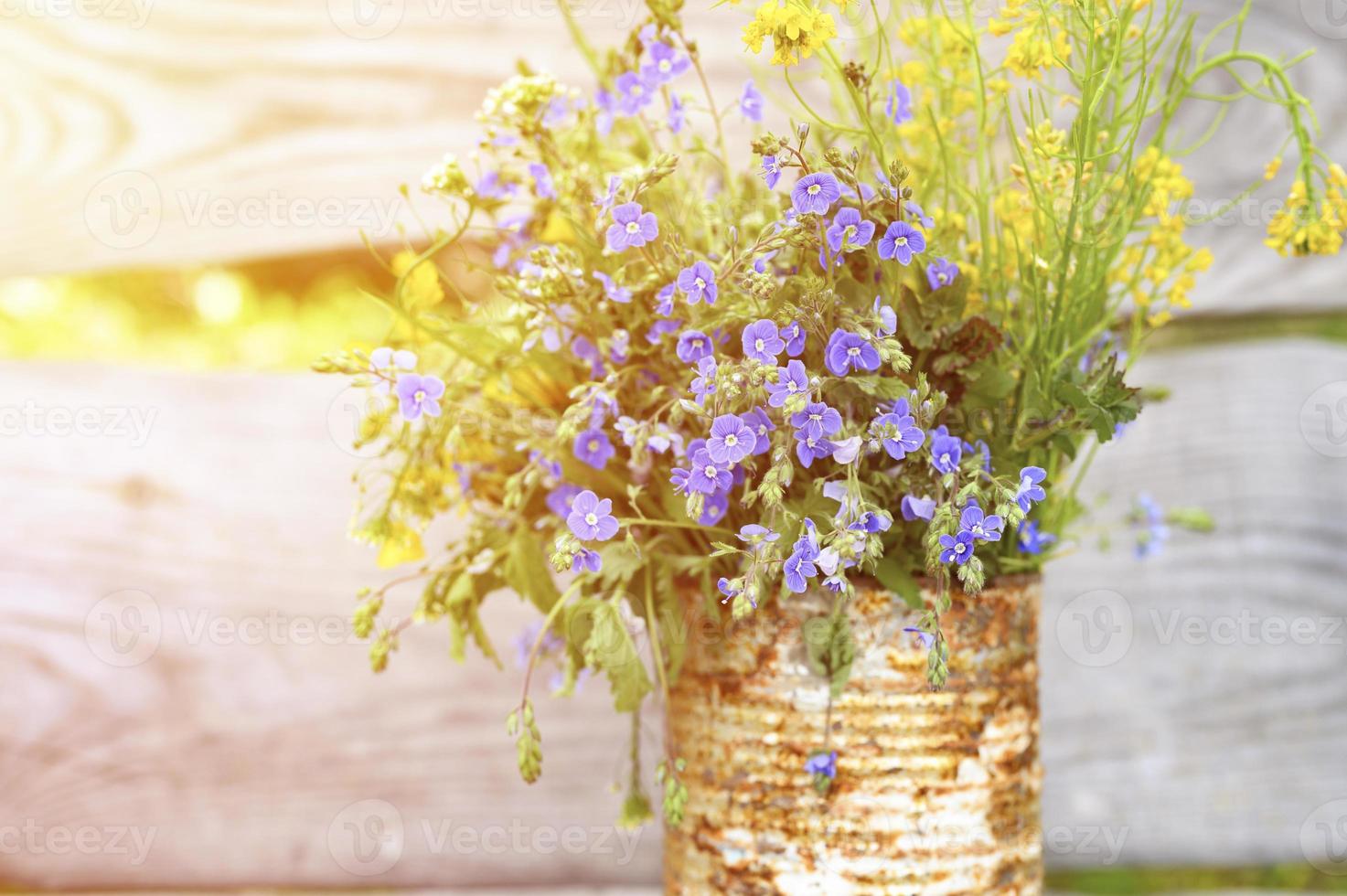 Ein Strauß Wildblumen aus Vergissmeinnicht, Gänseblümchen und gelbem Löwenzahn in voller Blüte in einem rustikalen Glas foto