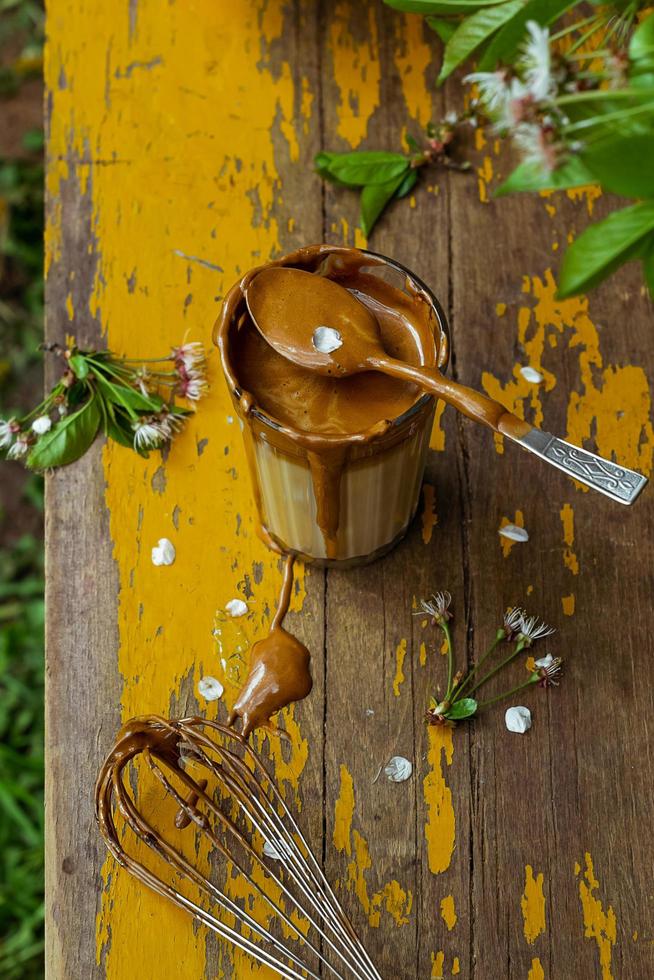 koreanischer Dalalgona-Kaffee in einem Glas, das an einem Frühlingstag auf einem alten gelben Gartentisch serviert wird foto