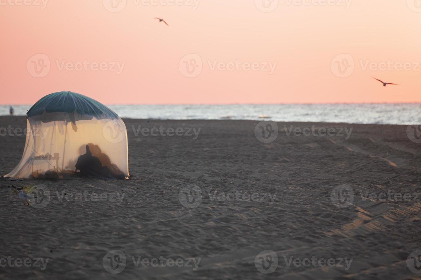 entspannen auf das Strand im ein Zelt. das Küste und das Silhouetten von Menschen im das Zelt. foto