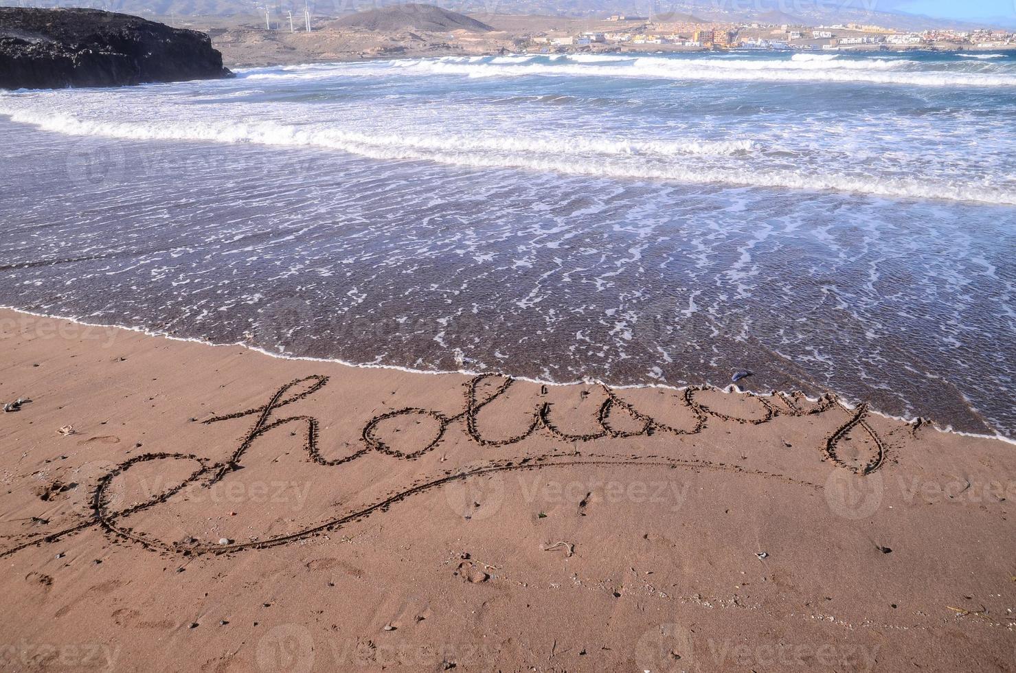 das Wort Urlaub geschrieben im das Sand foto
