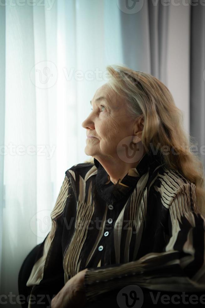 einsam alt Frau sitzen und aussehen aus das Fenster wo das Morgen Sonne scheint In. Fräulein meine geliebt Einsen Wer haben gewesen zusammen zum ein lange Zeit, Wer haben bestanden Weg ohne je Kommen zurück. foto