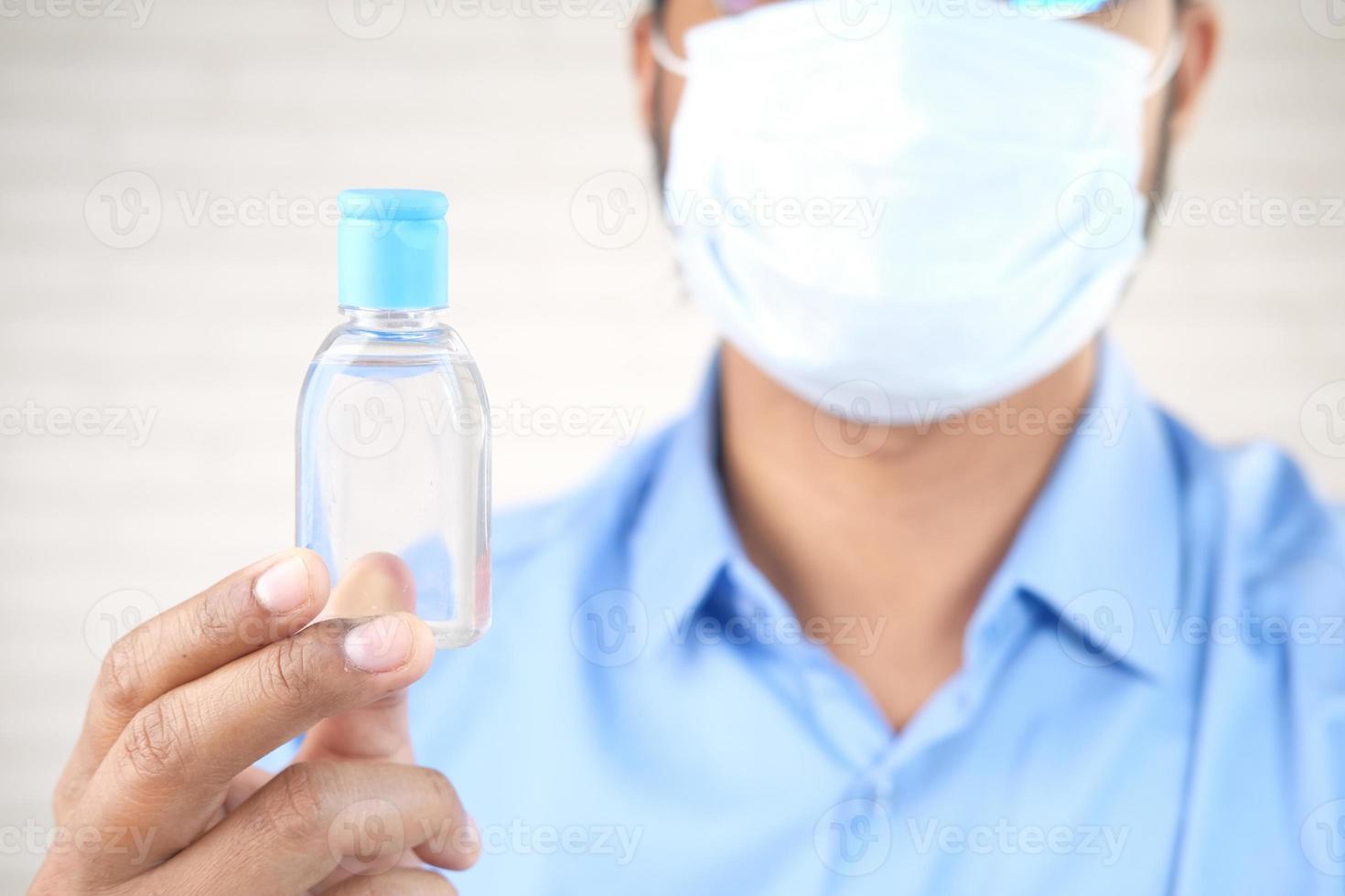 Mann, der Maske hält Händedesinfektionsmittelflasche hält foto