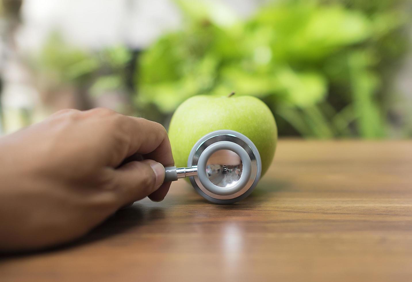 grüner Apfel mit einer Hand, die ein Stethoskop, Gesundheitskonzept hält foto