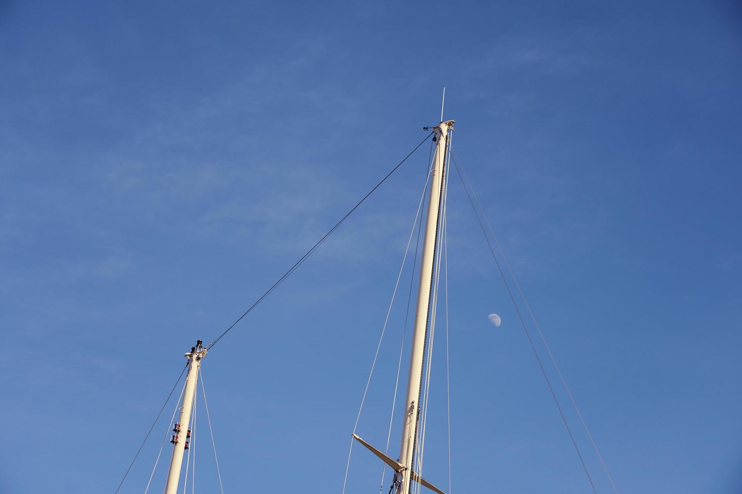 Yachtmasten gegen einen blauen Himmel mit dem Mond foto