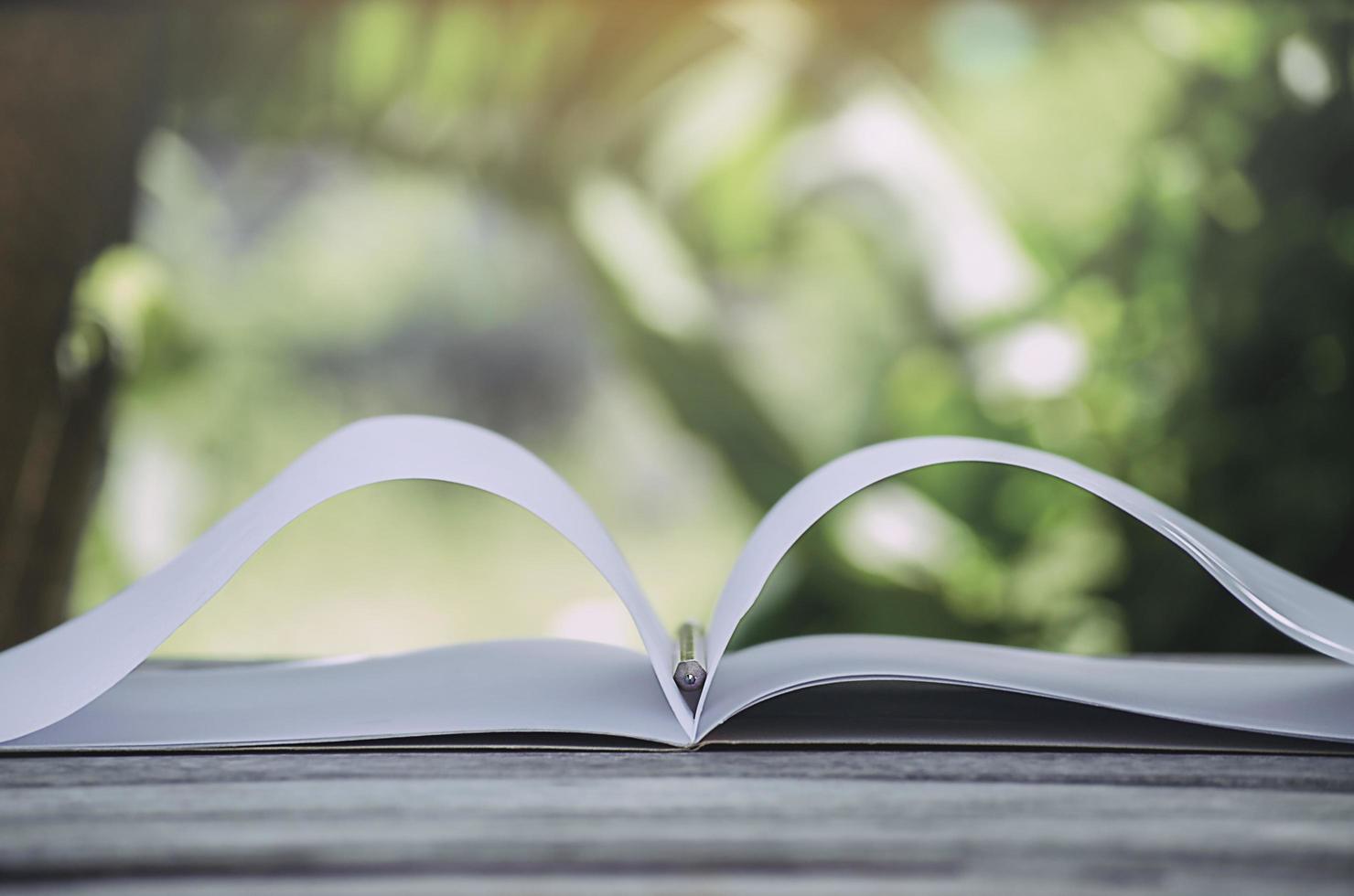 weißes Notizbuch und Bleistift auf einer Holzoberfläche mit einem unscharfen Naturhintergrund foto