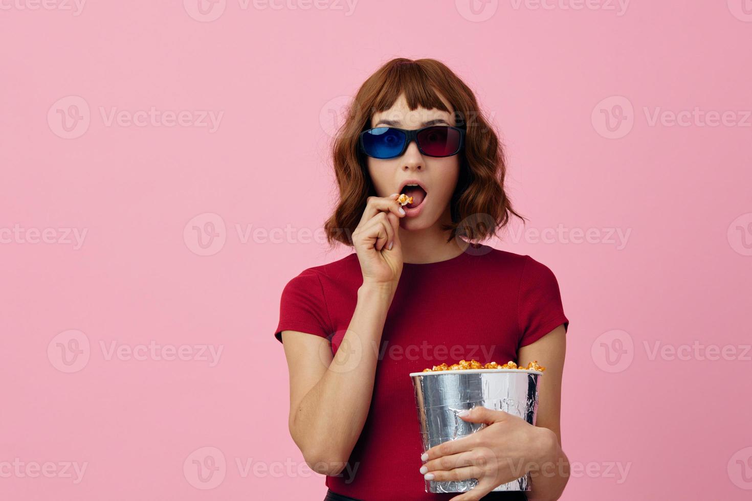 verwirrt konzentriert süß Rothaarige Dame im rot T-Shirt 3d Brille Essen Popcorn Uhr Film posieren isoliert auf Über Rosa Studio Hintergrund. Kopieren Raum Banner. Mode Kino Konzept. Unterhaltung Angebot foto