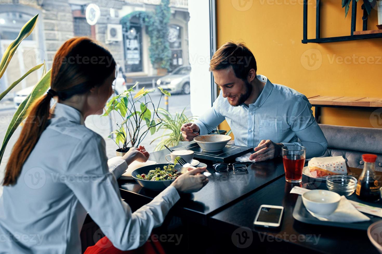 ein Mann und ein Frau im ein Hemd haben Abendessen beim ein Tabelle im ein Restaurant Innere im das Hintergrund heiß Essen Getränke foto