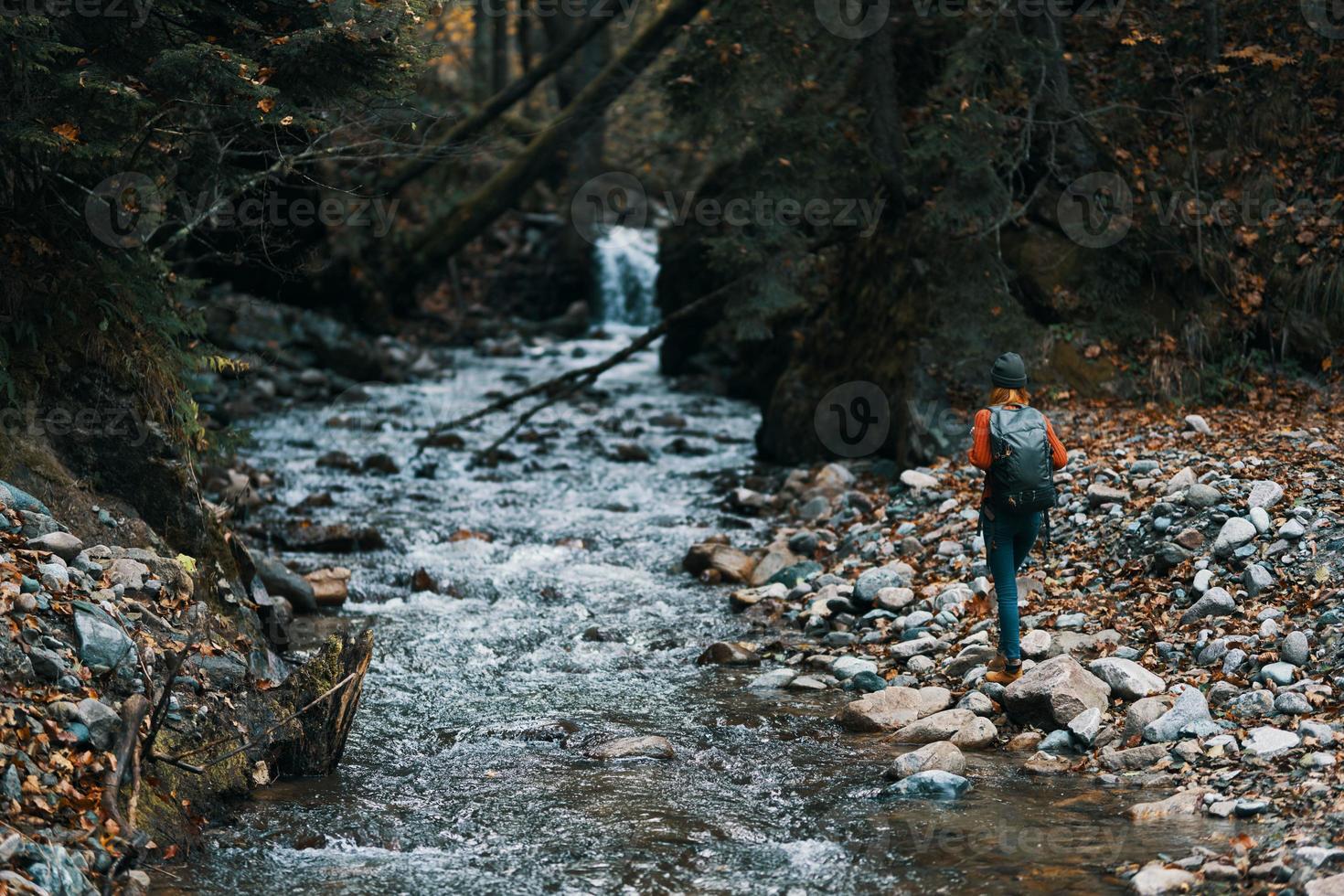 Frau Tourist mit ein Rucksack ging entlang das Bank in der Nähe von das Fluss, ein Strom von Wasser und hoch Bäume foto