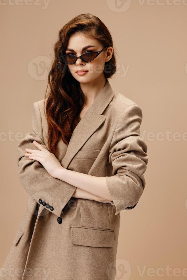 romantisch Frau im ein Mantel und Brille auf ein Beige Hintergrund suchen nach vorne foto