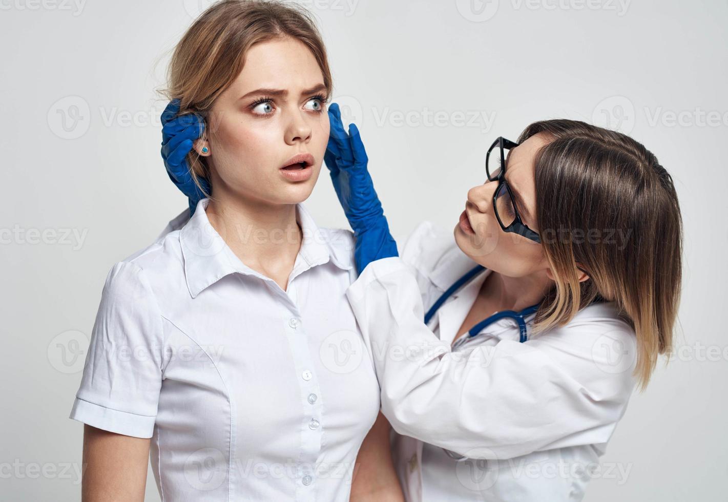 ein Frau Arzt im ein medizinisch Kleid und Blau Handschuhe untersucht das Patienten Gesicht foto