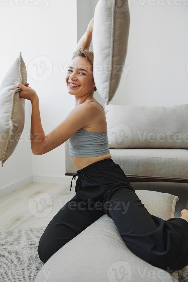 Teenager Mädchen Lächeln jedermann sitzt beim Zuhause in der Nähe von das Couch und wirft oben Kissen, Spaß Spiel und Glück ohne Filter, Kopieren Platz foto