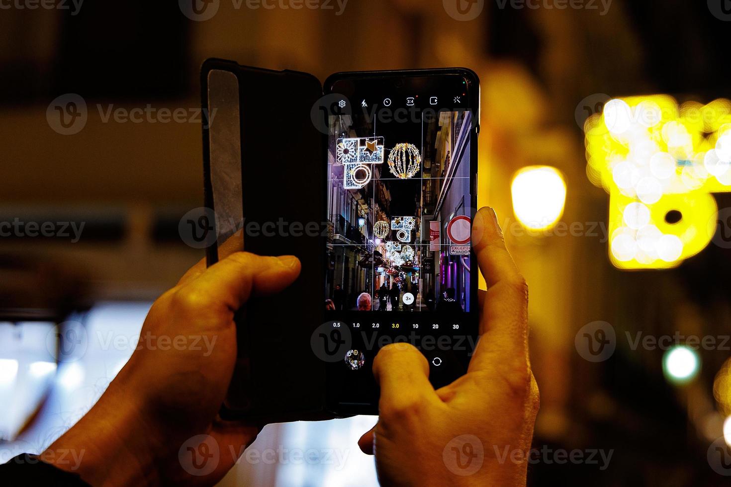 des Mannes Hände mit ein Handy, Mobiltelefon Telefon nehmen Bilder von das Weihnachten Straße beim Nacht foto