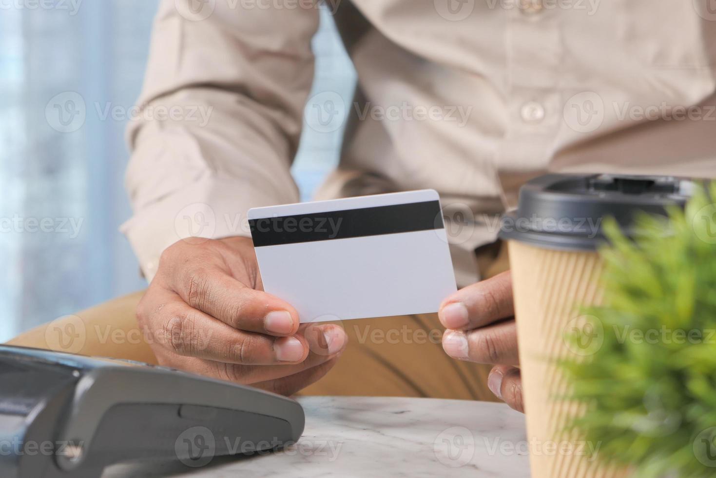 Mann, der weiße Kreditkarte mit schwarzem Streifen in einem Café hält foto