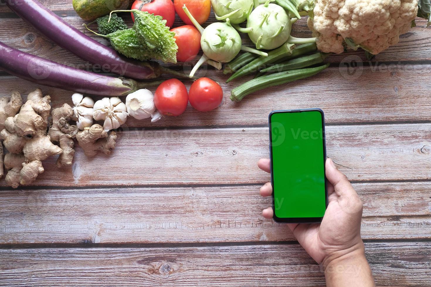 Smartphone mit grünem Bildschirm auf hölzernem Hintergrund mit viel frischem Gemüse foto