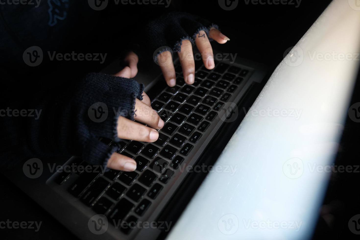 Mann mit Handschuhen, die auf dunkler Tastatur tippen foto