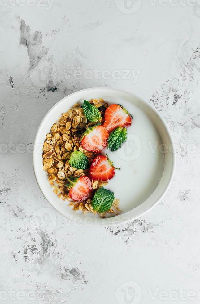 gesund Frühstück Essen minimal Konzept. Schüssel mit Granola, Joghurt und Beeren auf Weiß Marmor Hintergrund. oben Sicht, eben legen, Kopieren Raum foto