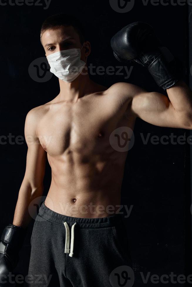 Boxer im ein medizinisch Maske auf ein schwarz Hintergrund Handschuhe Athlet nackt Torso Modell- foto